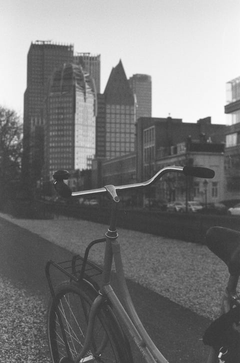 Black-and-white view of a bicycle's handlebars before a city skyline of tall office towers.