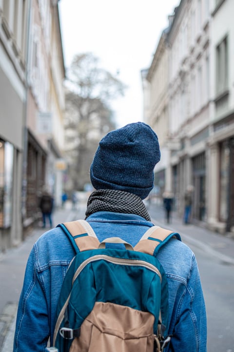 A person in a hooded jacket walking down a narrow city street.
