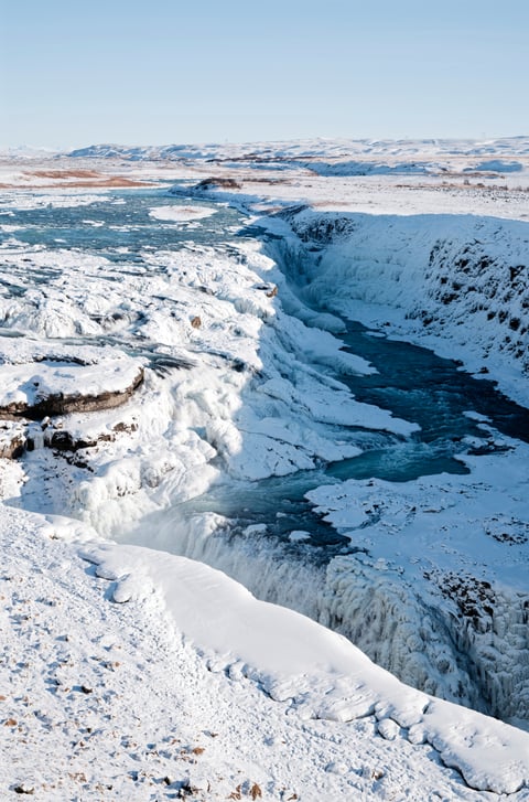 A snow- and ice-covered river canyon winding toward the horizon under a clear blue sky.