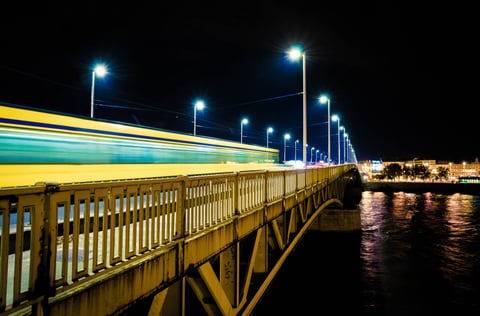 A bridge at night with blue lights and long yellow light trails.