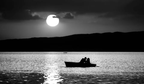 Black and white lake scene with a small boat under a bright sun.