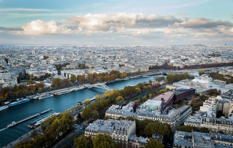Aerial view over a city and river beneath broken clouds.